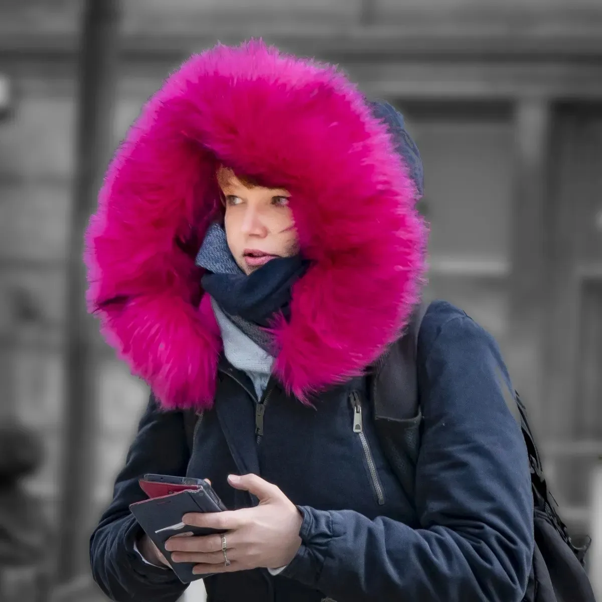 Woman with a vivid pink fur hood holding a phone and wallet